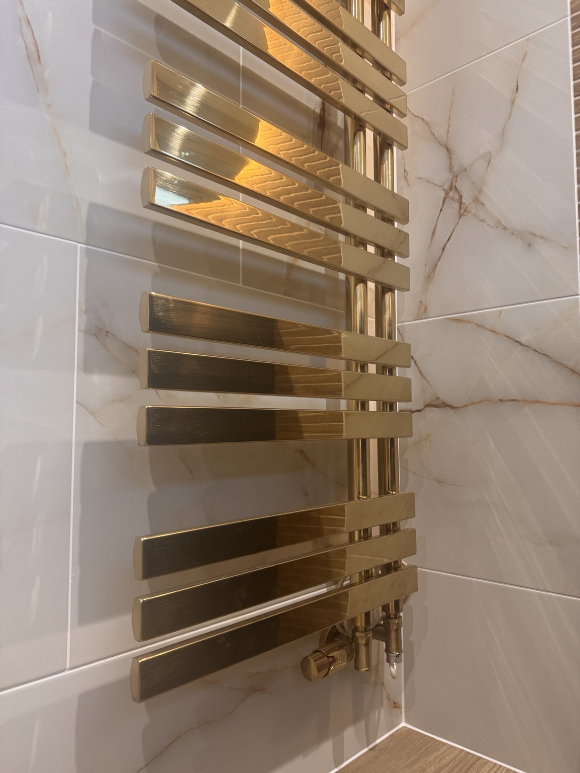 Brass towel radiator against marble-effect tiles