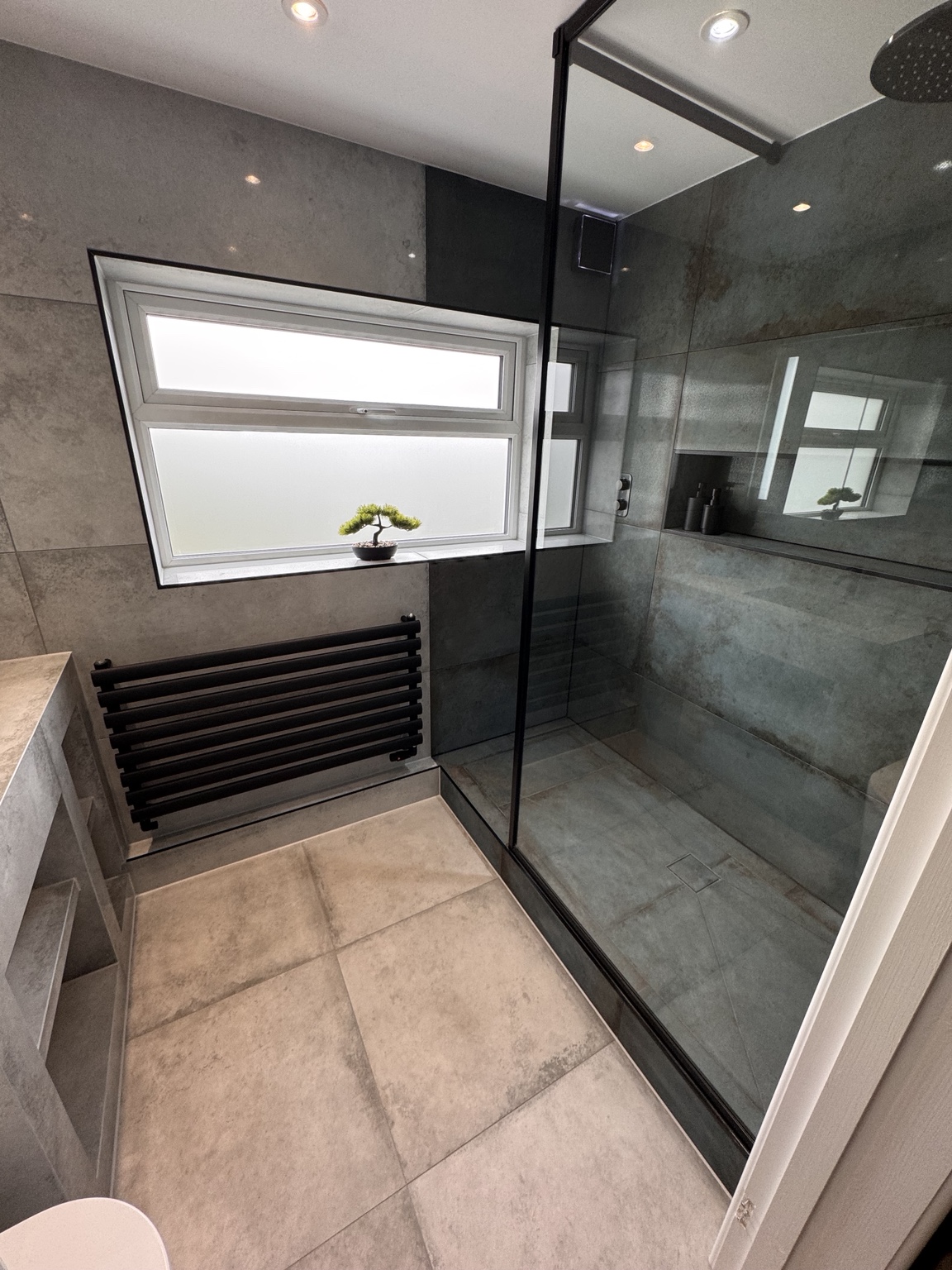 Wet room shower screen, tiled floor and black heated towel rail